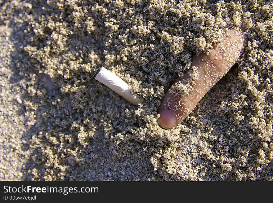 Finger with cigarette half buried in the sands. Finger with cigarette half buried in the sands