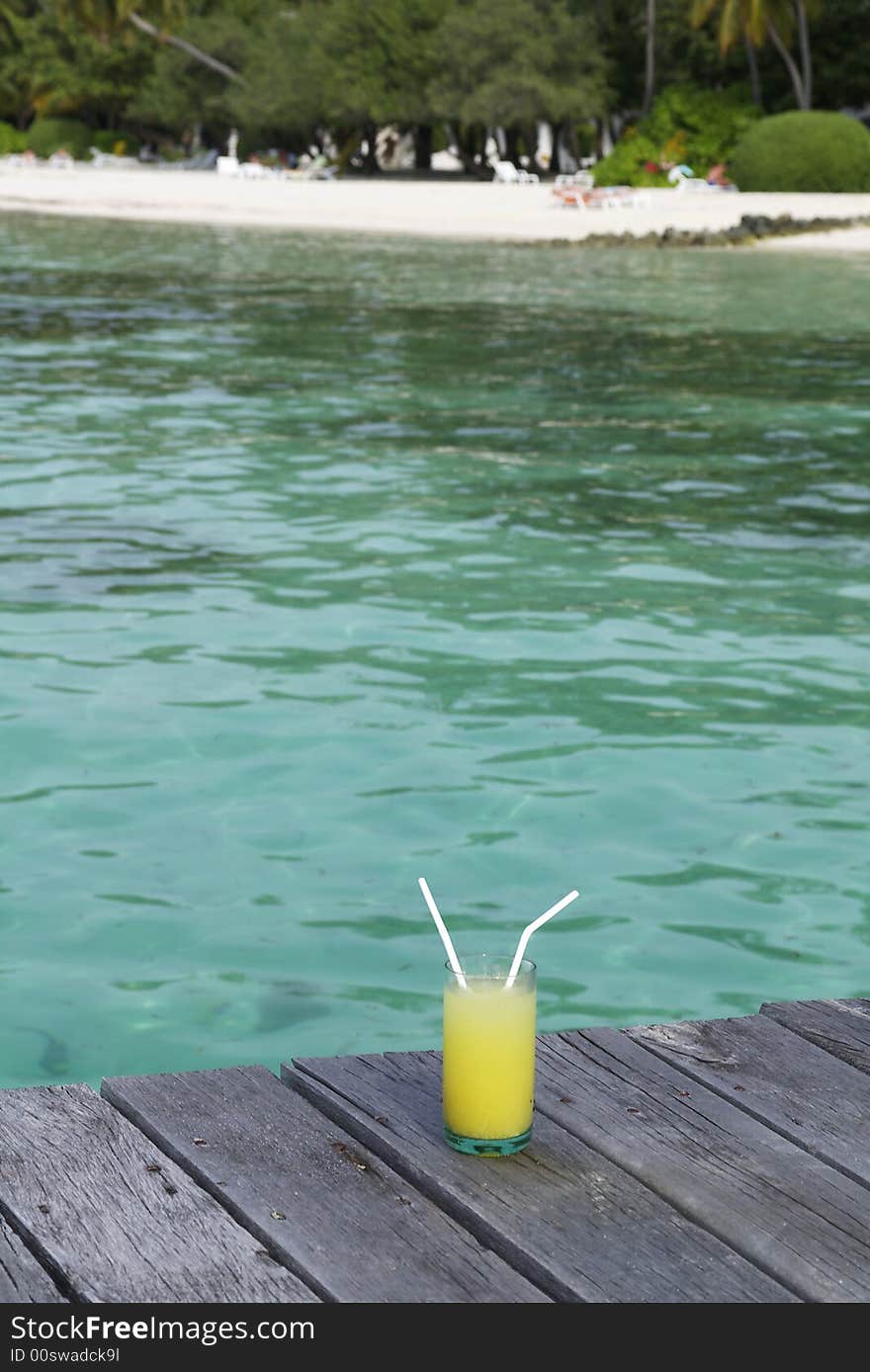 Drink in a glass with 2 straws with a beach in the background. Drink in a glass with 2 straws with a beach in the background.