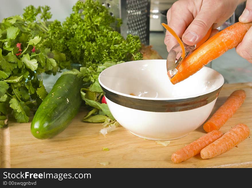 Carrots Being Peeled Against Backdrop of Kitchen Utensils and Other Vegetables. Carrots Being Peeled Against Backdrop of Kitchen Utensils and Other Vegetables