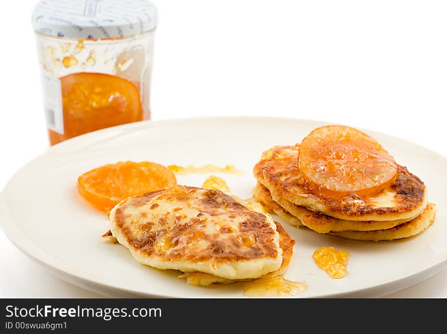 Small 
cottage pancakes with some orange jam, jam jar in background, isolated on white. Small 
cottage pancakes with some orange jam, jam jar in background, isolated on white