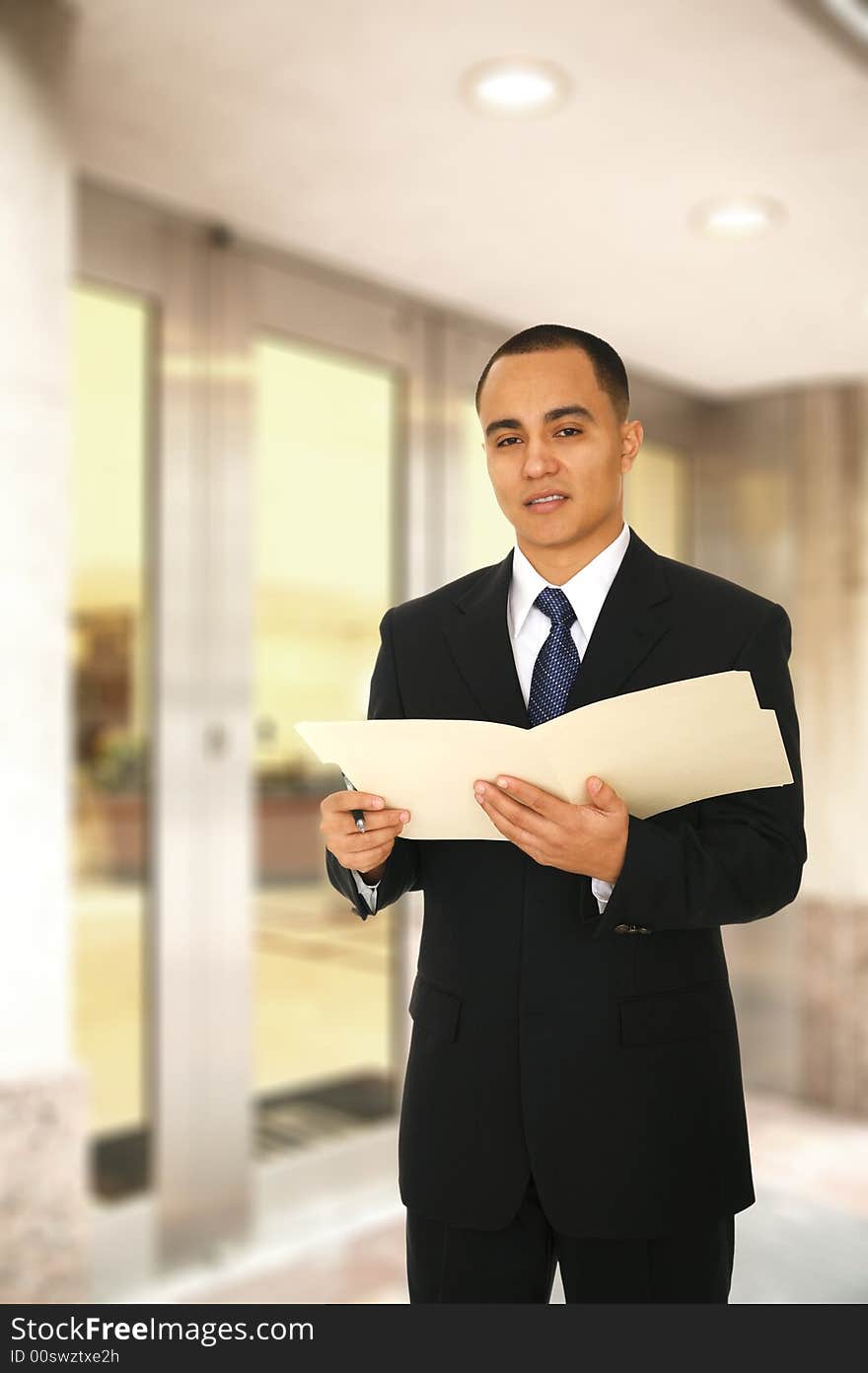 A man holding folder and looking at camera while walking out from his office main entrance. A man holding folder and looking at camera while walking out from his office main entrance