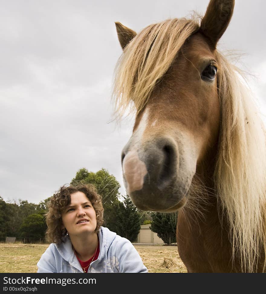 Teenage girl sitting on the ground looking at her pony. Teenage girl sitting on the ground looking at her pony