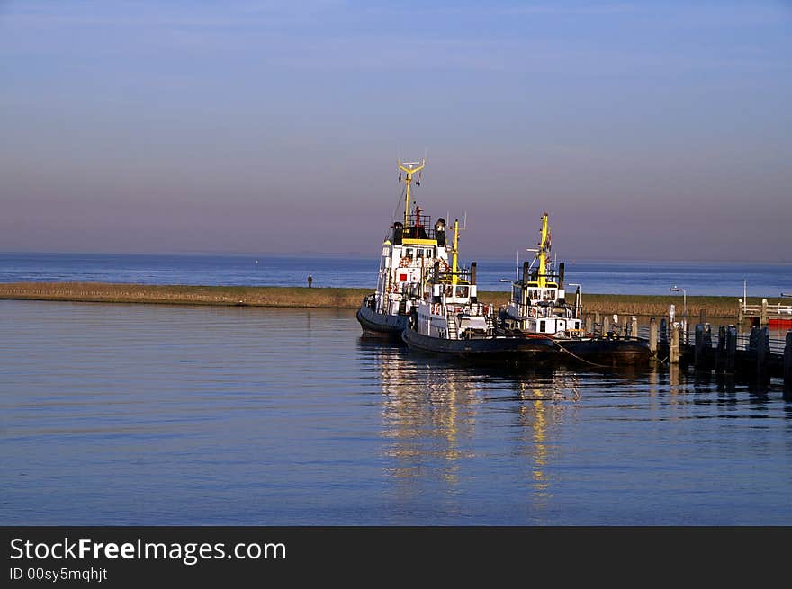 Tugboats tied to pier on water against blue sky. Tugboats tied to pier on water against blue sky