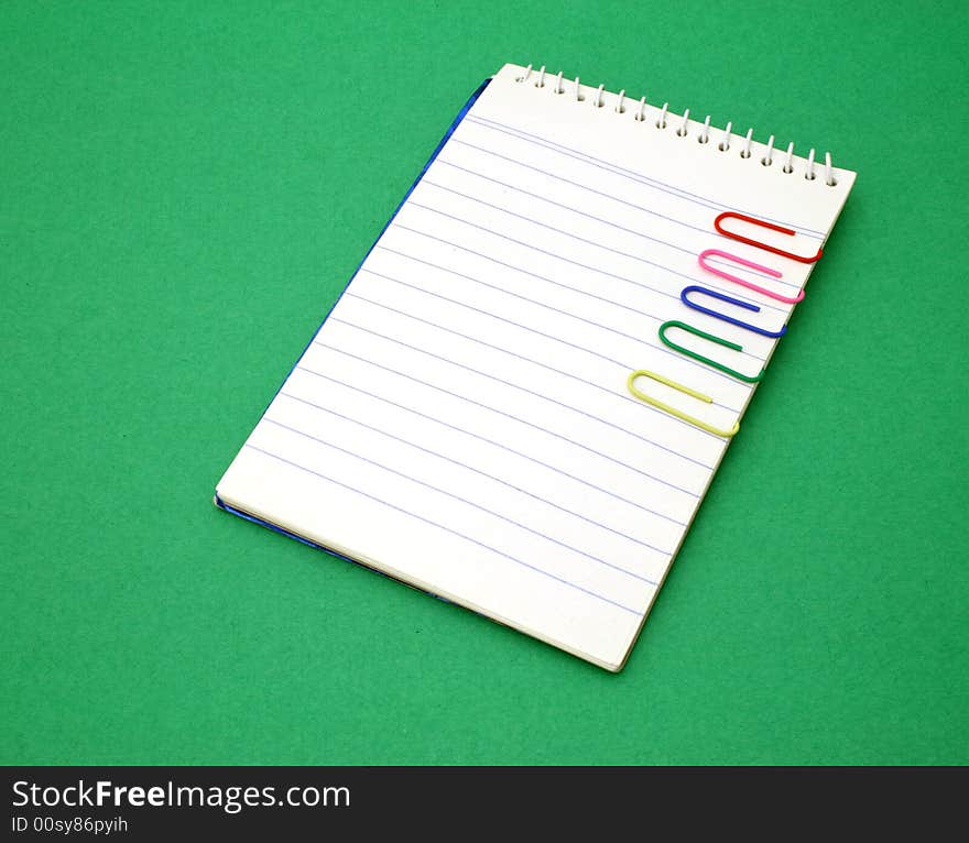 Open notebook with several paper clips over a green surface. Open notebook with several paper clips over a green surface