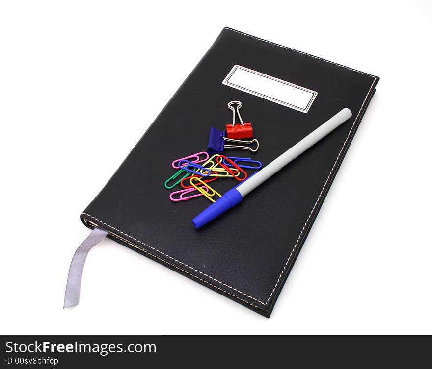 Pen and paper clips over a black journal in a white surface. Pen and paper clips over a black journal in a white surface