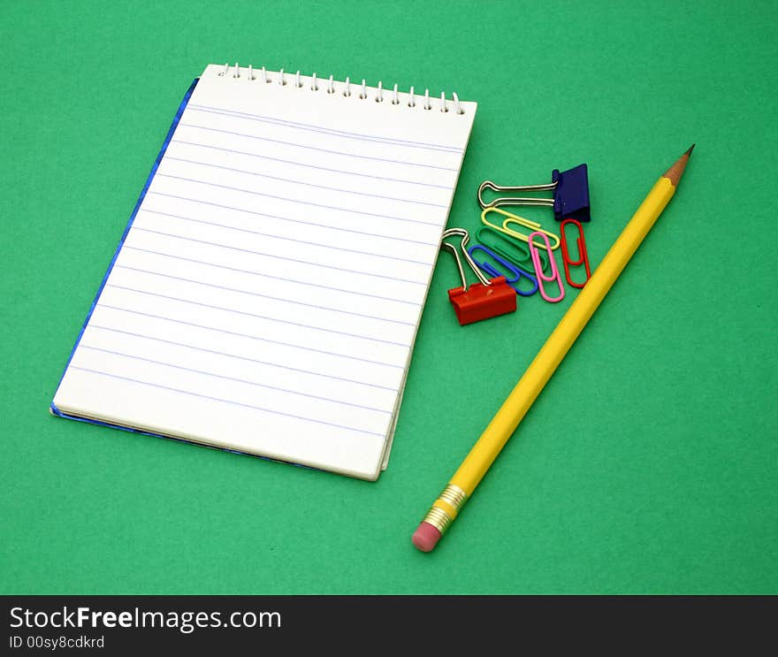 Yellow pen and paper clips besides an open notebook on a green surface. Yellow pen and paper clips besides an open notebook on a green surface