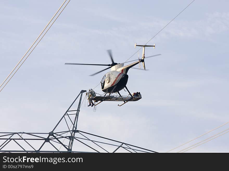 Contractors are installing new high voltage transmission towers to carry electricity across the country, final work is done with worker sitting on bench below helicopter on the skids making final connections to high voltage lines. Contractors are installing new high voltage transmission towers to carry electricity across the country, final work is done with worker sitting on bench below helicopter on the skids making final connections to high voltage lines