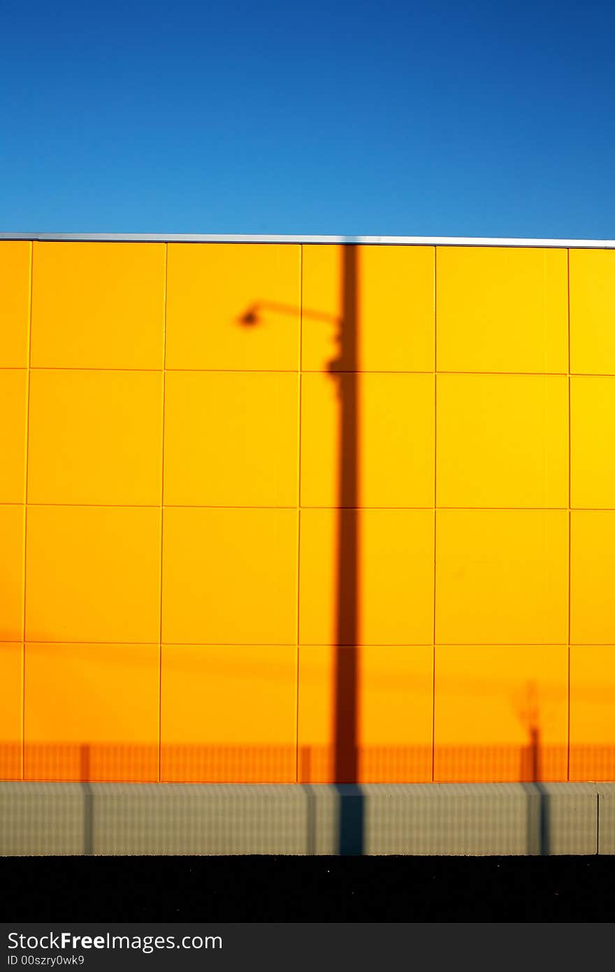 Urban landscape: modern yellow wall with lampost shadow