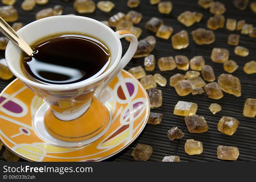 Colorful cup of coffee full of black coffee surrounded by cubes of crystallized brown sugar. Room for copy on the right.