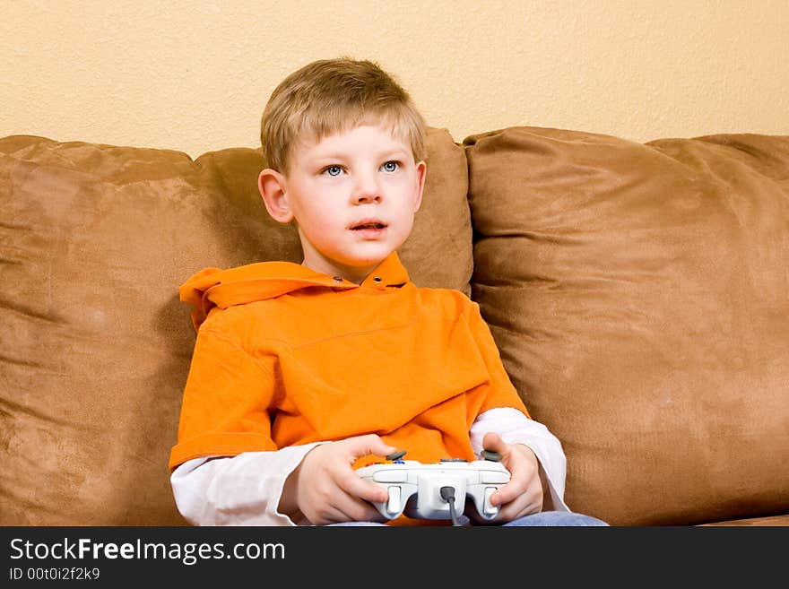 Here is a photo of a young boy sitting on a couch playing a video game. Here is a photo of a young boy sitting on a couch playing a video game.