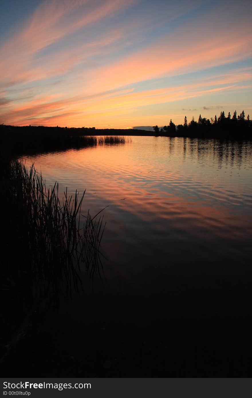 Sunset over a calm lake with a silhouetted forest and shore. Sunset over a calm lake with a silhouetted forest and shore