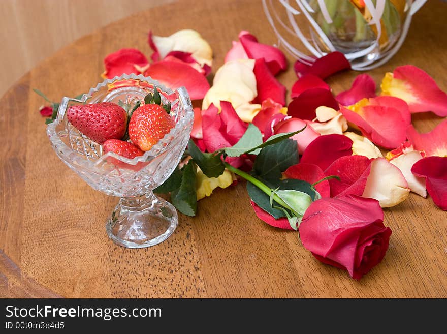 Strawberry in a vase, red rose on the table and petals of red roses. Strawberry in a vase, red rose on the table and petals of red roses