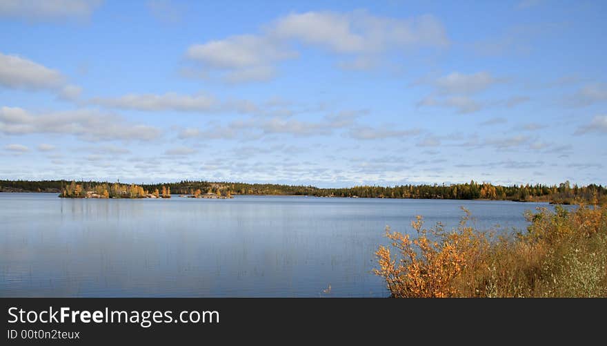 Landscape of a forest reflection in a calm Autumn lake with big blue sky. Landscape of a forest reflection in a calm Autumn lake with big blue sky