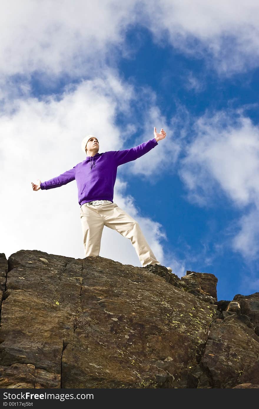 Young man on the rocks in defiant gesture. Young man on the rocks in defiant gesture