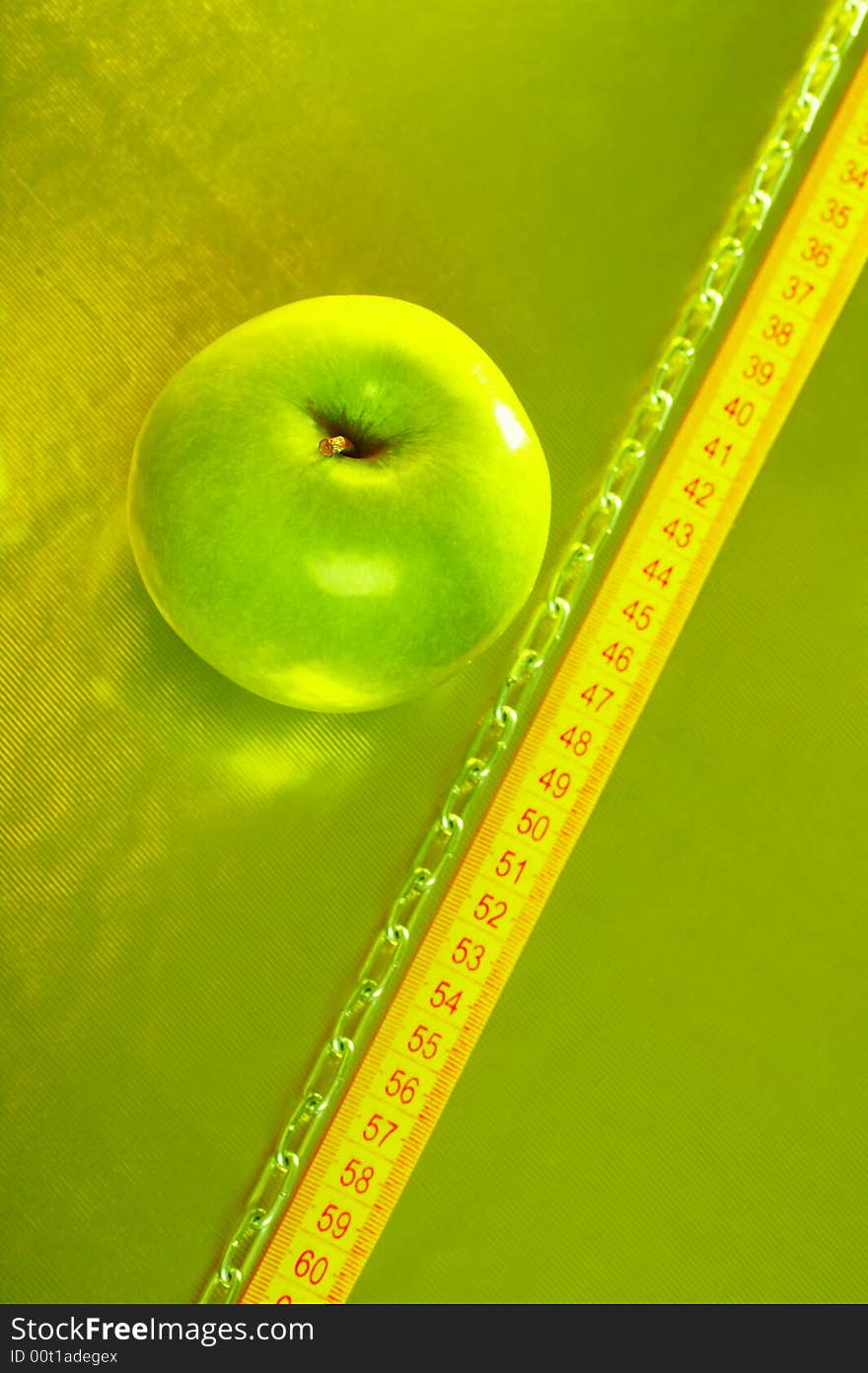 The green apple lays on a gold background with tape measure and a chain. The green apple lays on a gold background with tape measure and a chain