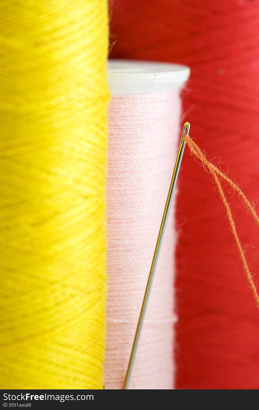 Threads in yellow, pink and red close up. Focus on needle with orange thread.