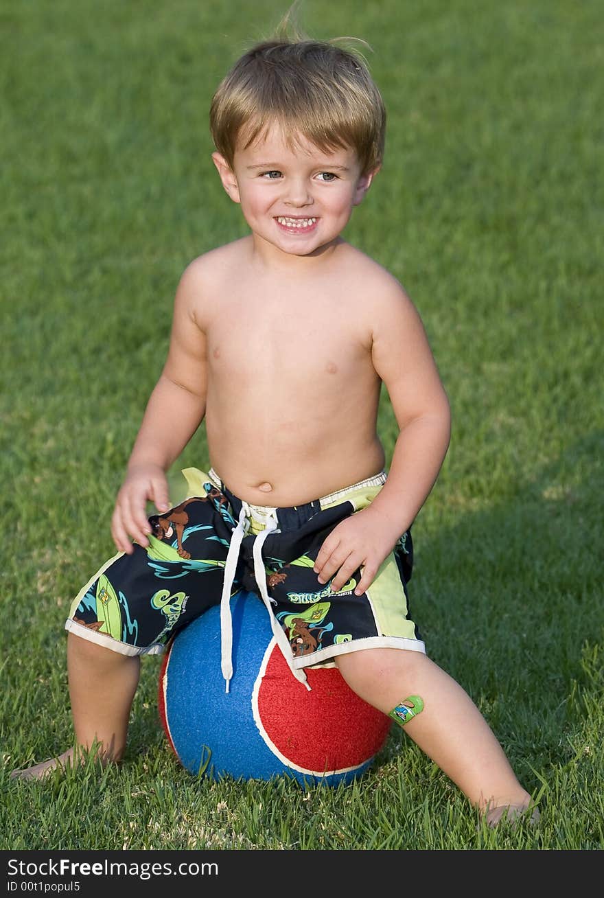 Young boy sitting on a very large blue and red tennis ball. Young boy sitting on a very large blue and red tennis ball