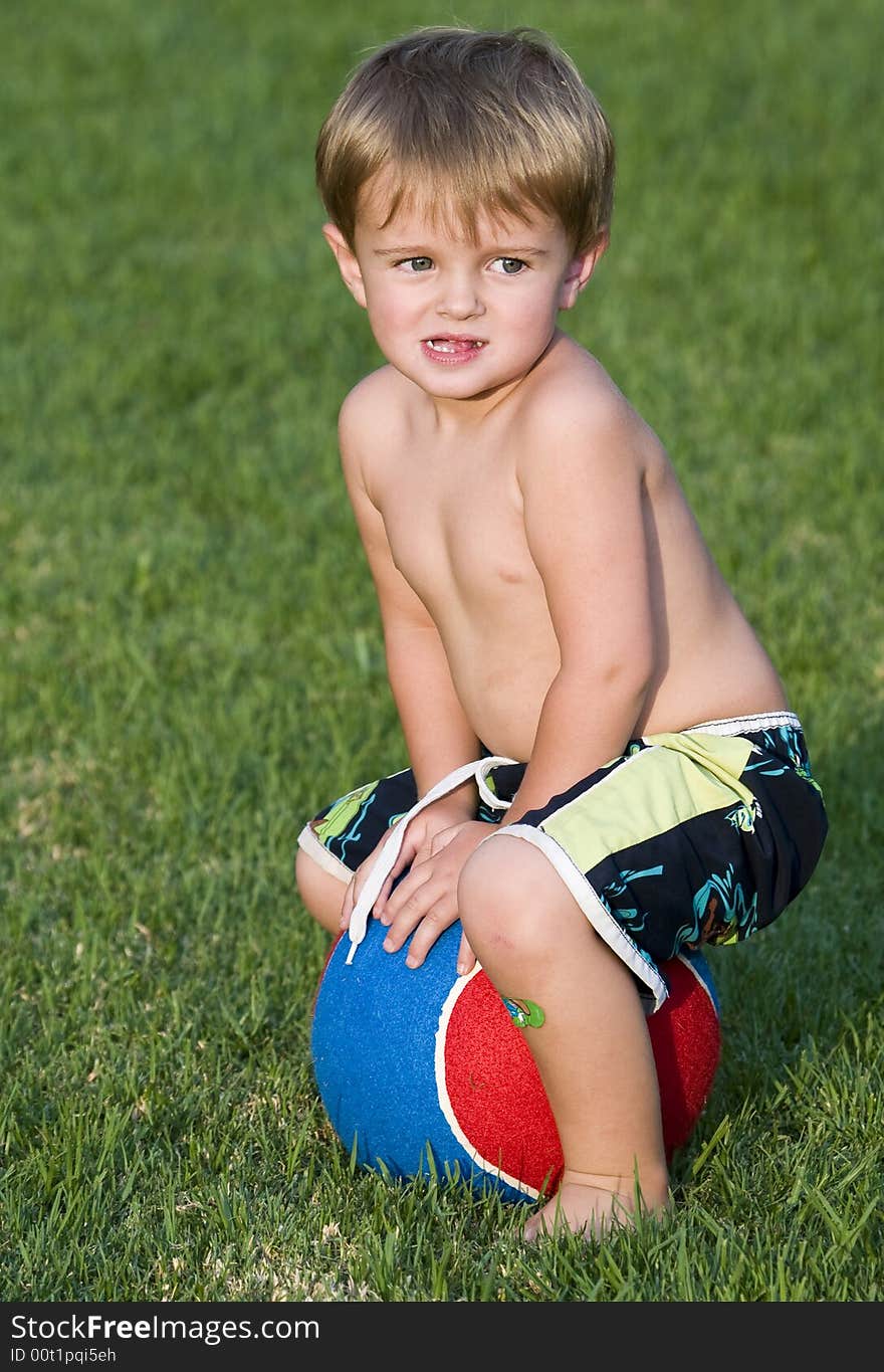 Young boy sitting on a very large blue and red tennis ball. Young boy sitting on a very large blue and red tennis ball