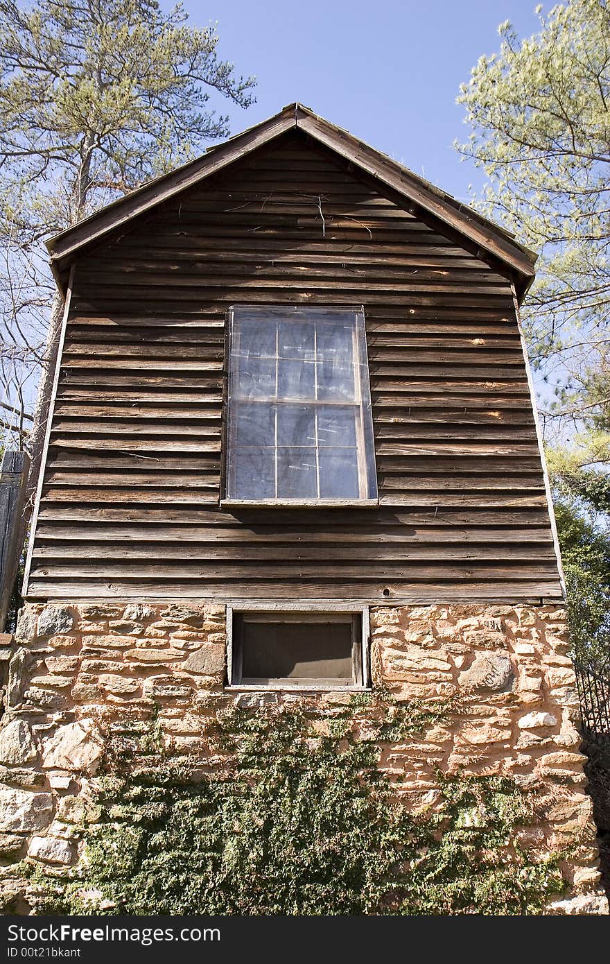 An old plank and log house on a stone foundation against a blue sky. An old plank and log house on a stone foundation against a blue sky