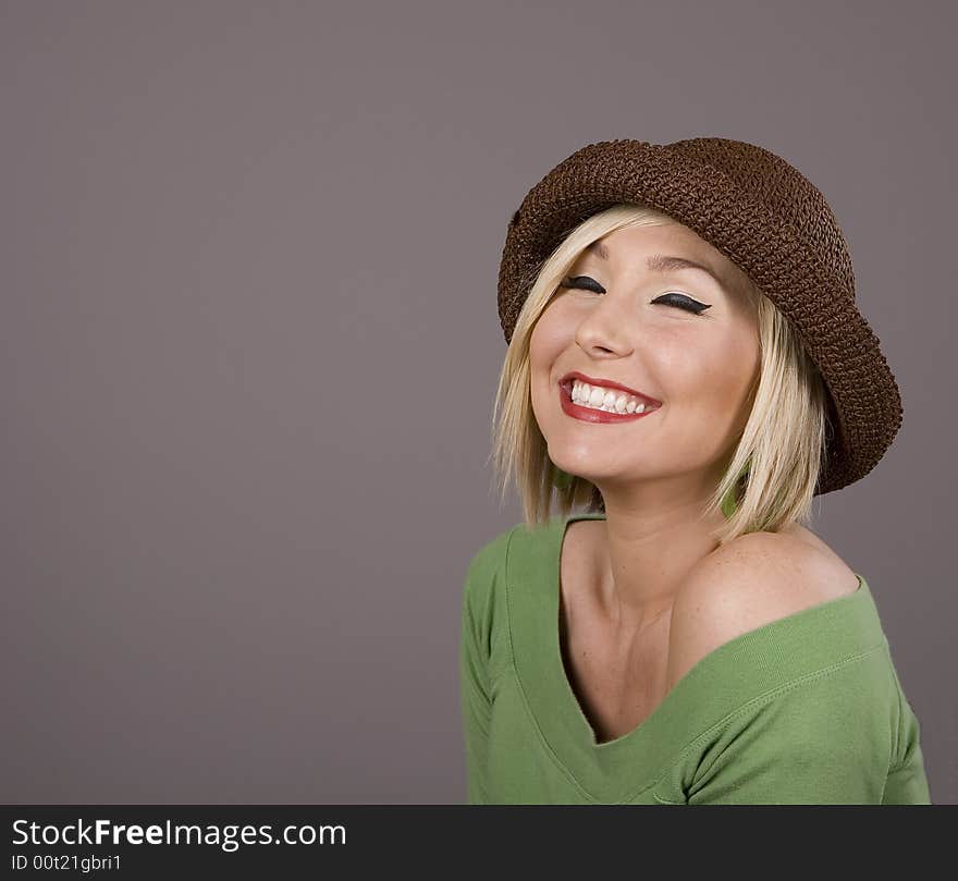 A blonde in a green blouse and a brown hat with eyes closed and a smile. A blonde in a green blouse and a brown hat with eyes closed and a smile