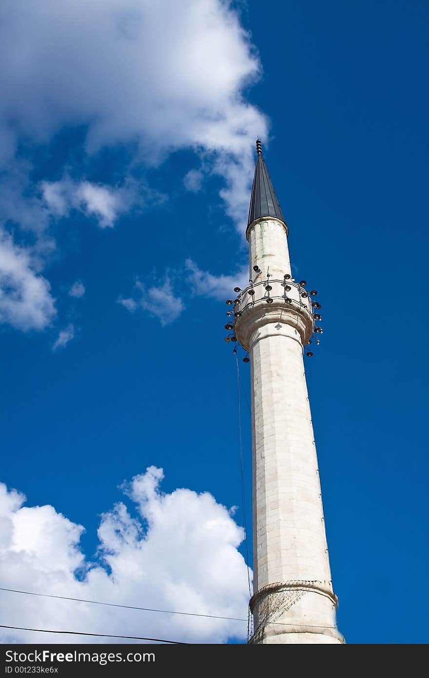 Single minaret of the mosque under the blue and cloudy sky