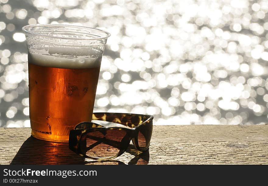 Glass of beer and a pair of sunglassas sitting on a deck handrail overlooking the ocean. Glass of beer and a pair of sunglassas sitting on a deck handrail overlooking the ocean