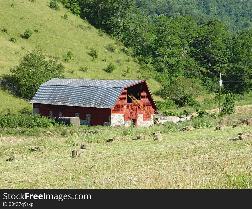 A red barn in a rural area with a hayfield