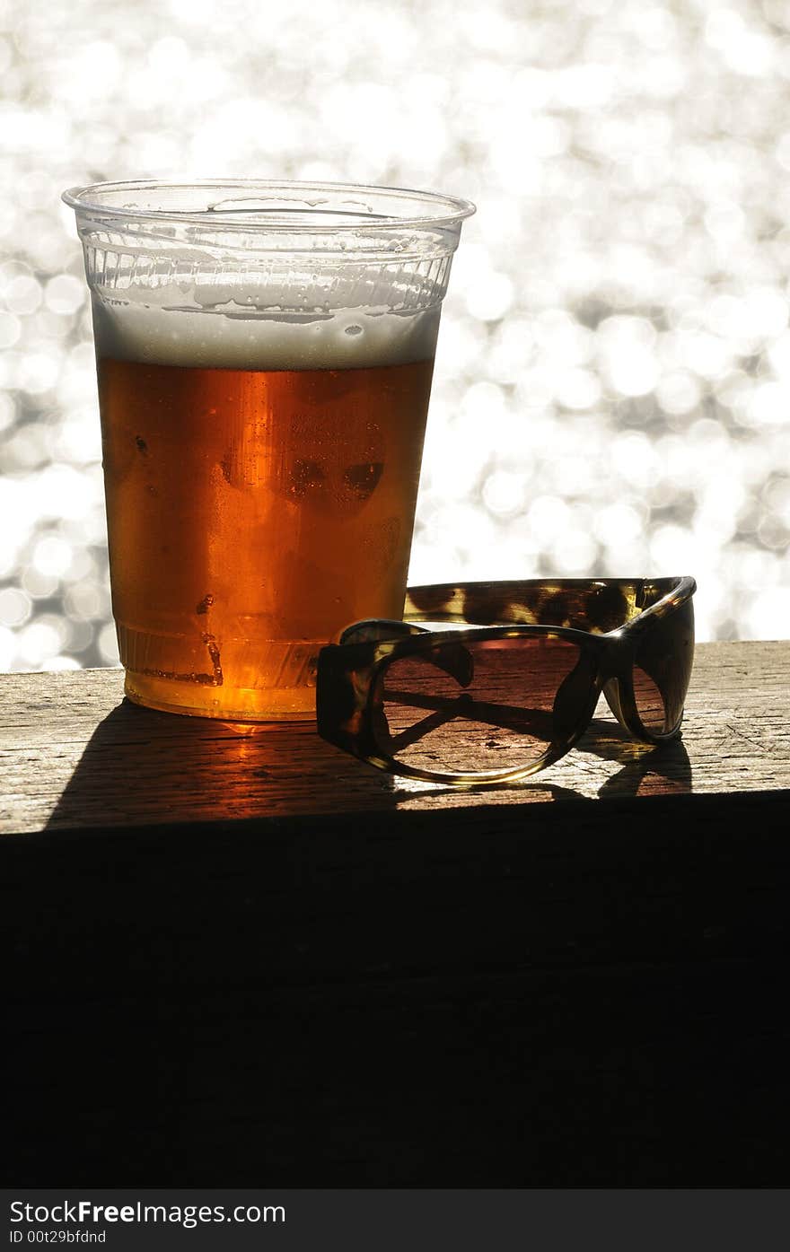 Glass of beer and a pair of sunglassas sitting on a deck handrail overlooking the ocean. Glass of beer and a pair of sunglassas sitting on a deck handrail overlooking the ocean