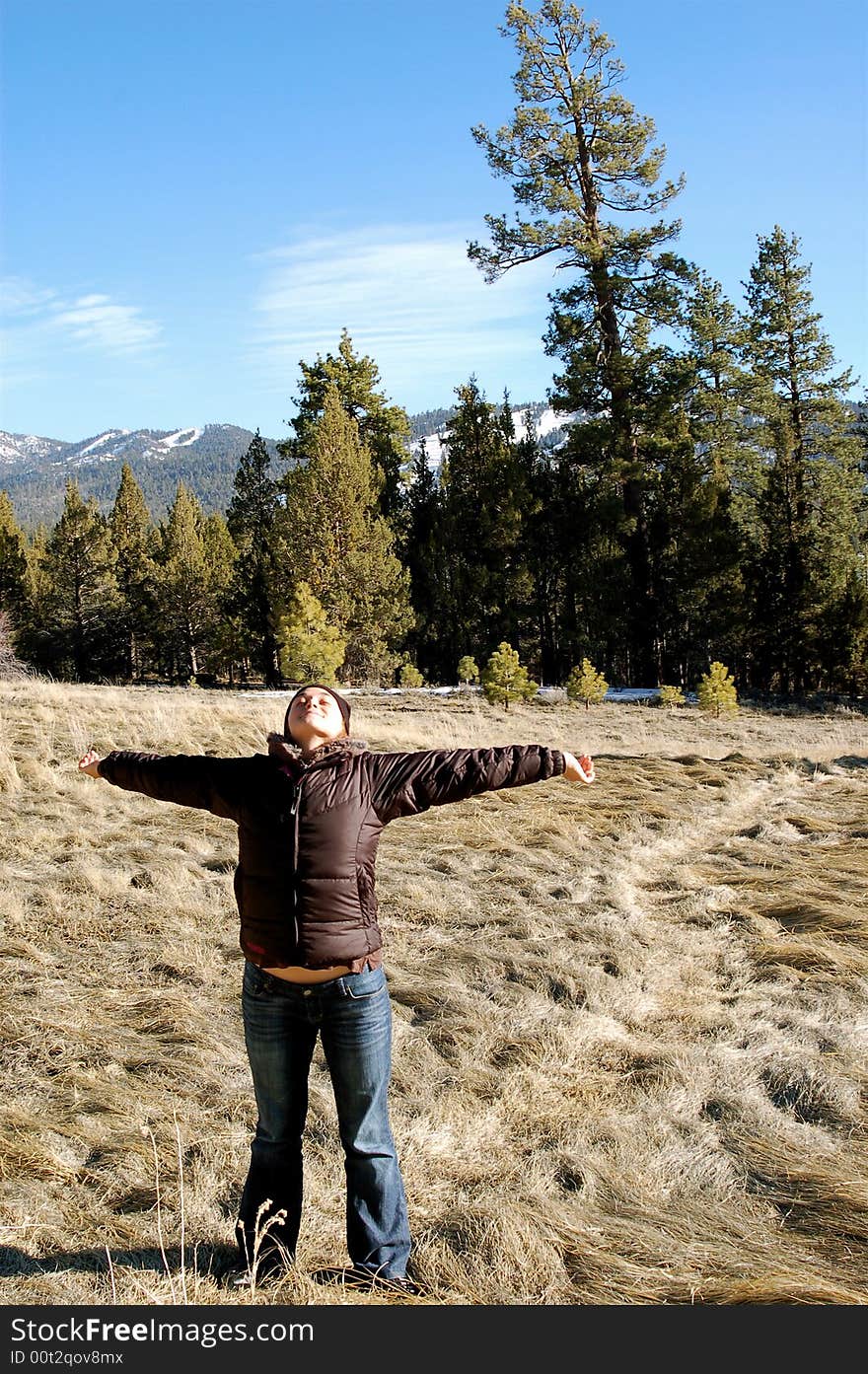 A woman stands in a field with open arms and trees and mountains in the background. A woman stands in a field with open arms and trees and mountains in the background.