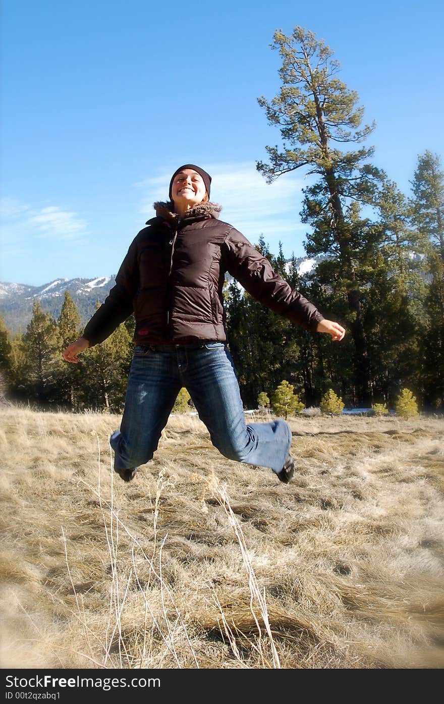 A woman jumps in a field with trees and mountains in the background. A woman jumps in a field with trees and mountains in the background.