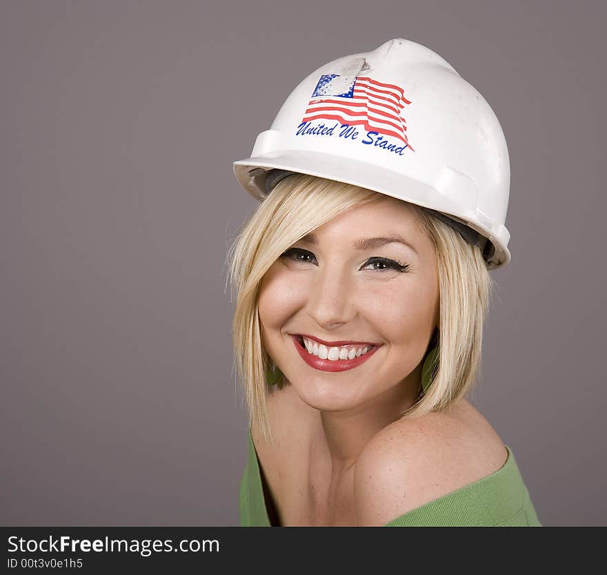 A blonde wearing a construction hard hat and smiling at the camera. A blonde wearing a construction hard hat and smiling at the camera