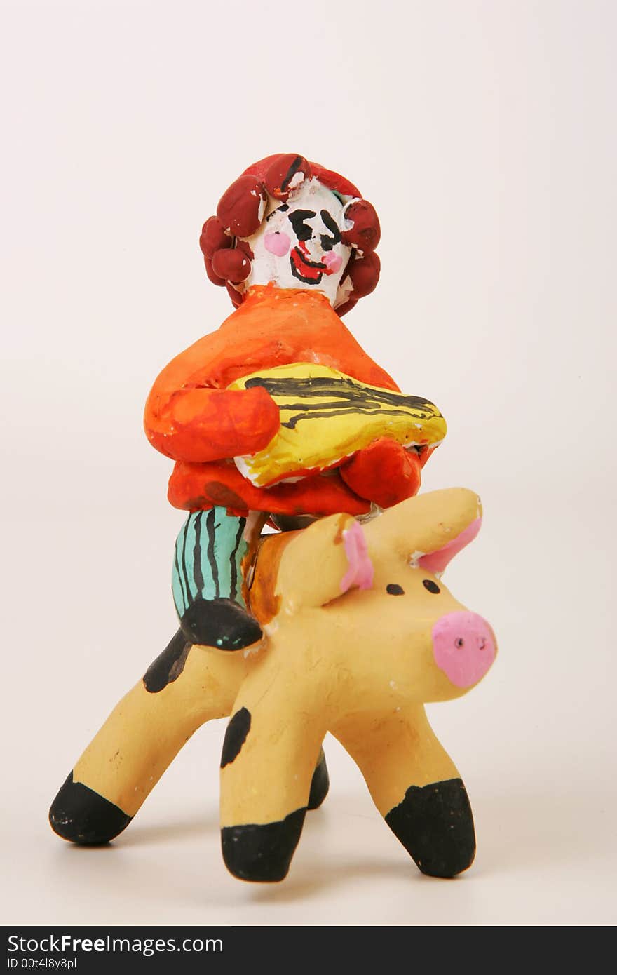 A painted clay figure of a merry musician riding a pig. A painted clay figure of a merry musician riding a pig