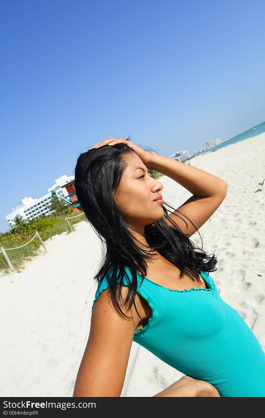 Woman at the beach with her hand on her head.