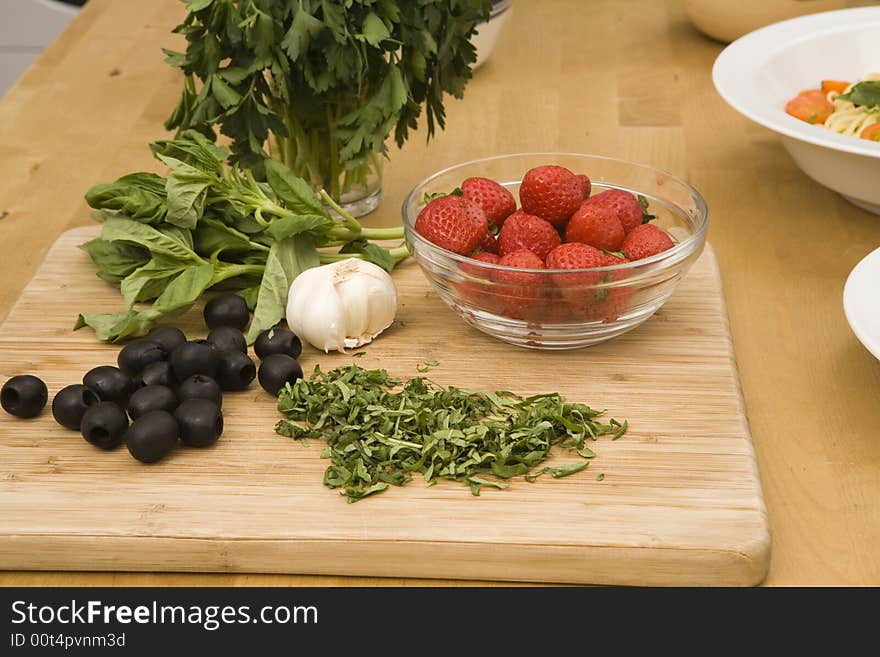 Strawberries inside a bowl, black olives, garlic and basil on top of a wood cutting board. Strawberries inside a bowl, black olives, garlic and basil on top of a wood cutting board.