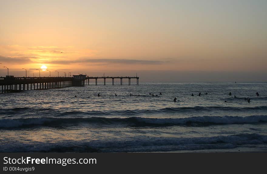 This is a photo of the Ocean Beach Pier in San Diego, California and many surfers waiting for surf as the sun is starting to set. This is a photo of the Ocean Beach Pier in San Diego, California and many surfers waiting for surf as the sun is starting to set.