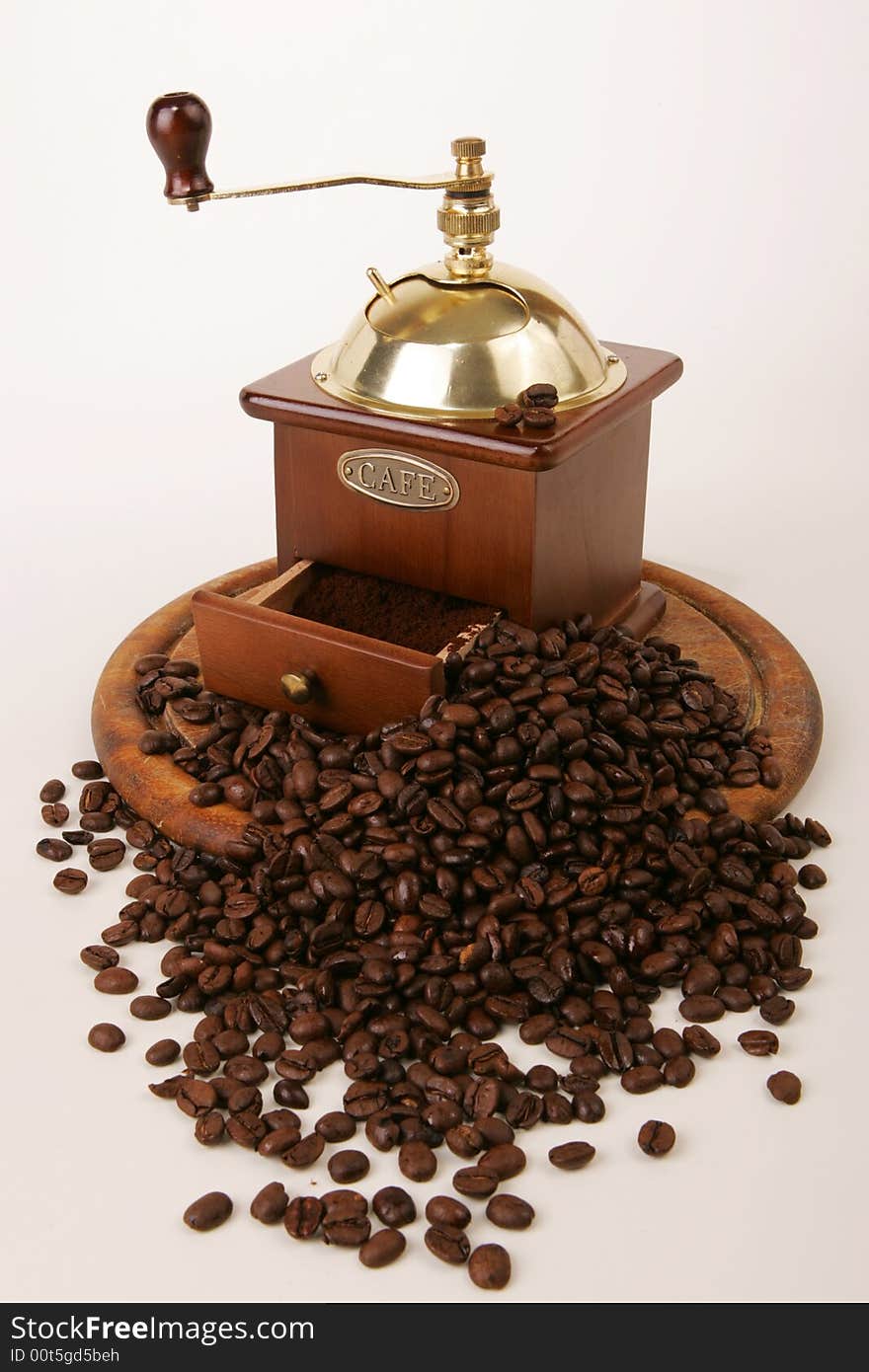 A coffee-mill on a wooden tray and spilt beans. A coffee-mill on a wooden tray and spilt beans