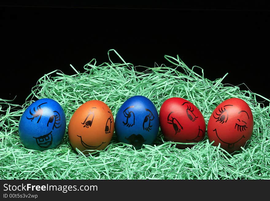 Colored eggs are standing with green on the black background. Colored eggs are standing with green on the black background