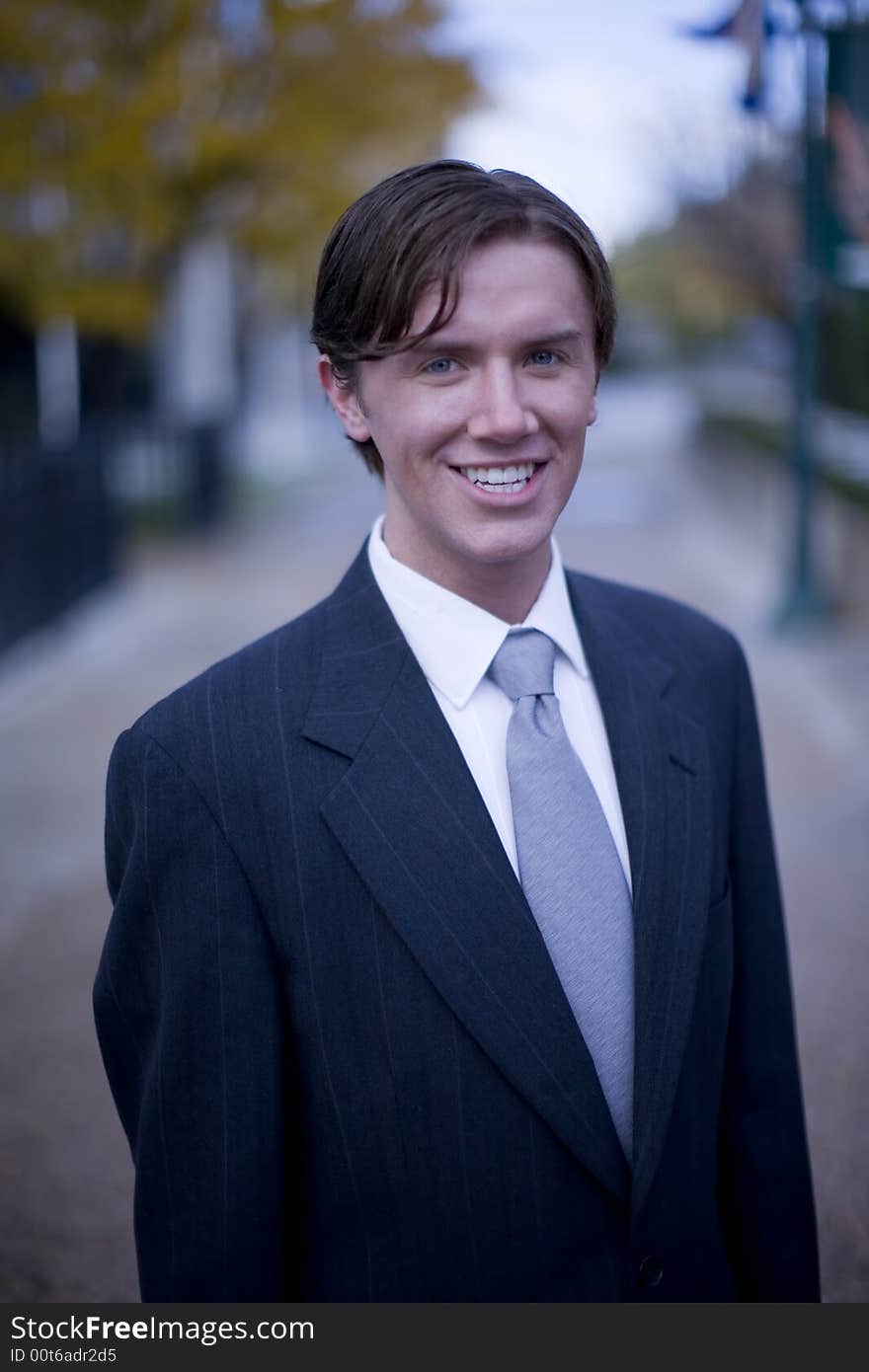 Front view of single white young businessman standing looking at camera with office buildings in background. Front view of single white young businessman standing looking at camera with office buildings in background