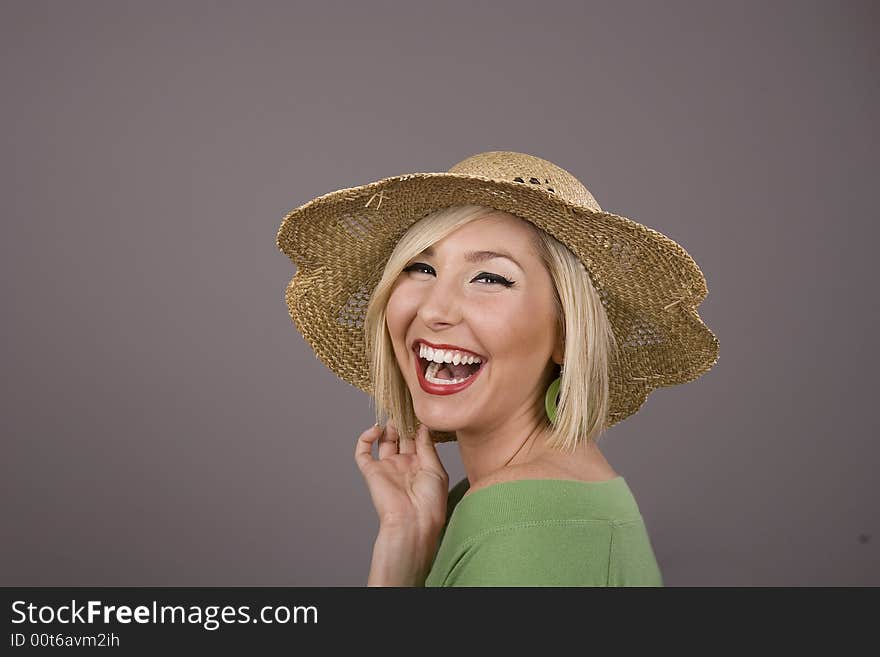 A blonde in a green blouse and a straw hat laughing against a grey background. A blonde in a green blouse and a straw hat laughing against a grey background