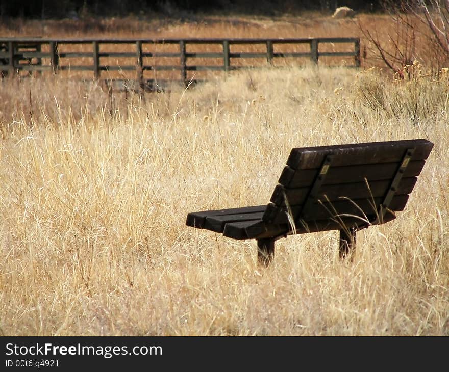 A wood bench in a field, on the bank of a river with a bridge in the background. A wood bench in a field, on the bank of a river with a bridge in the background.