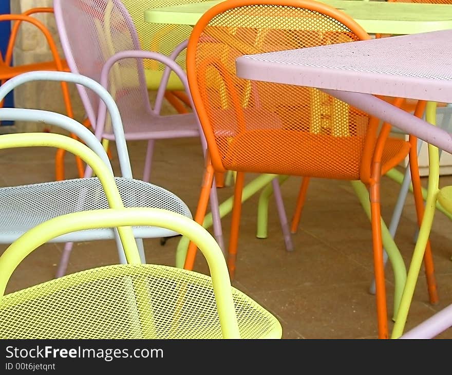 An arrangement of colorful cafe tables outside in the sun.