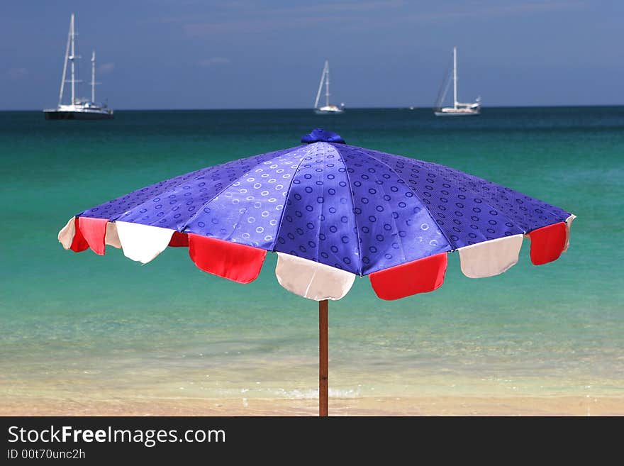 Bright blue and red beach umbrella overlooking the ocean on a summer day.