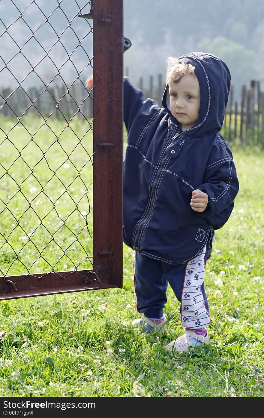 On a background mountains and green grass a little boy opens a metallic gate. On a background mountains and green grass a little boy opens a metallic gate