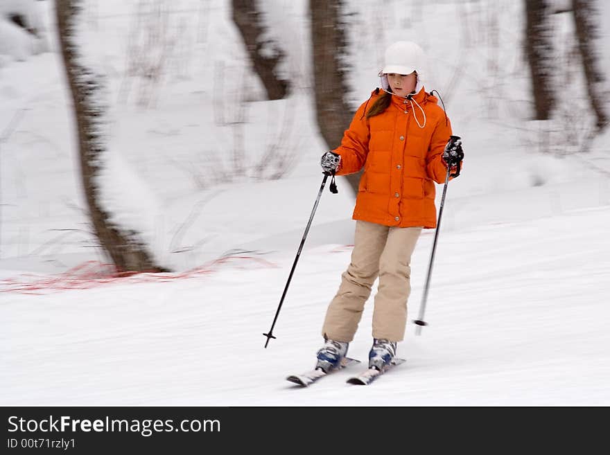 A girl-teenager in an orange jacket and white cap goes for a drive on mountain ski. A girl-teenager in an orange jacket and white cap goes for a drive on mountain ski