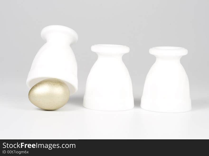 Three eggcups and gold egg on a white background. Concept for Thimblerig.