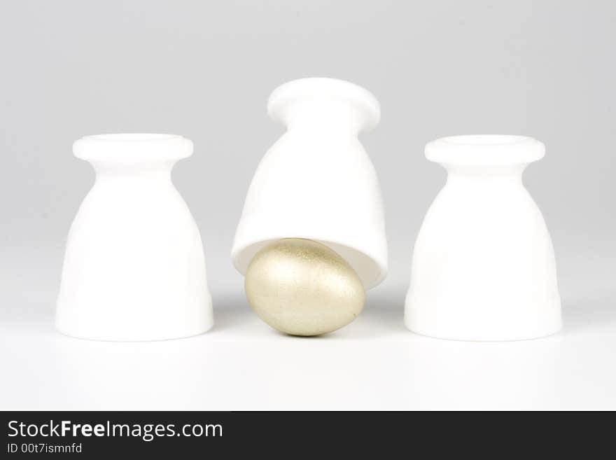 Three eggcups and gold egg on a white background. Concept for Thimblerig.