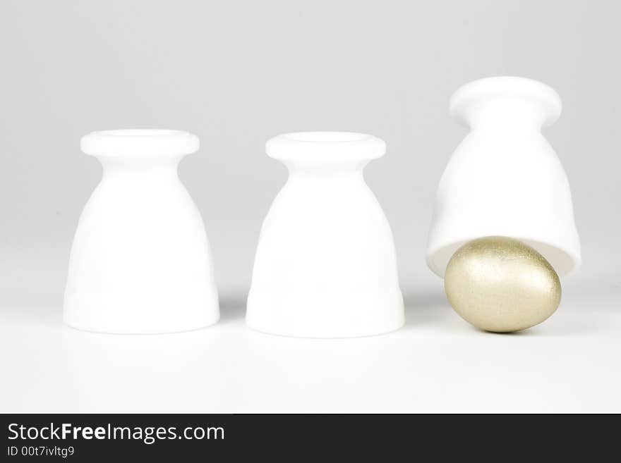 Three eggcups and gold egg on a white background. Concept for Thimblerig.