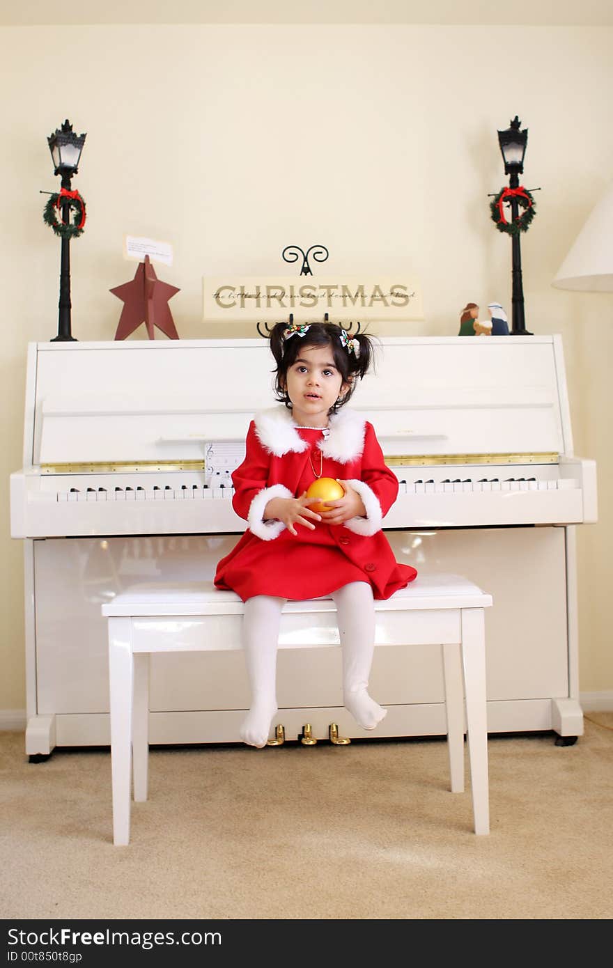 A child playing a white piano wearing a red dress