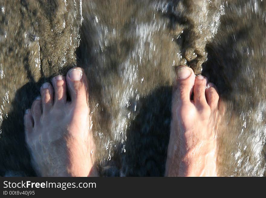 A pair of feet are touched by the sea. A pair of feet are touched by the sea