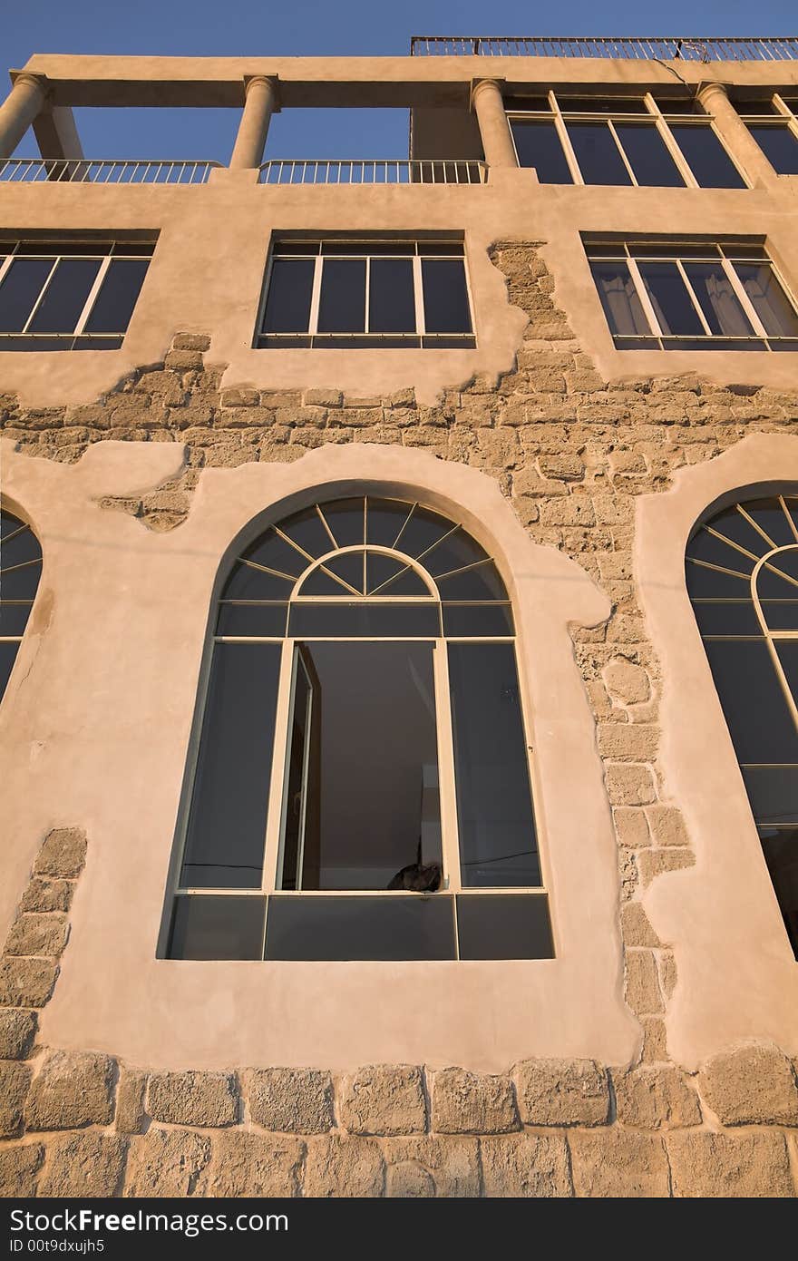 Glasses of windows of an ancient building sparkling on a sunset and a black dog sitting in a window. Glasses of windows of an ancient building sparkling on a sunset and a black dog sitting in a window